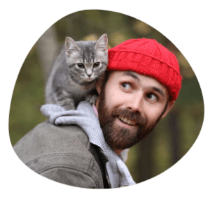 Cat Parent in grey jacket with red cap & grey cat on the shoulder is happy with Pawland’s cat sitters for personalised care