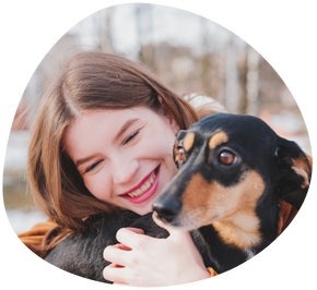 A smiling female dog sitter hugging a black dachshund in her hand