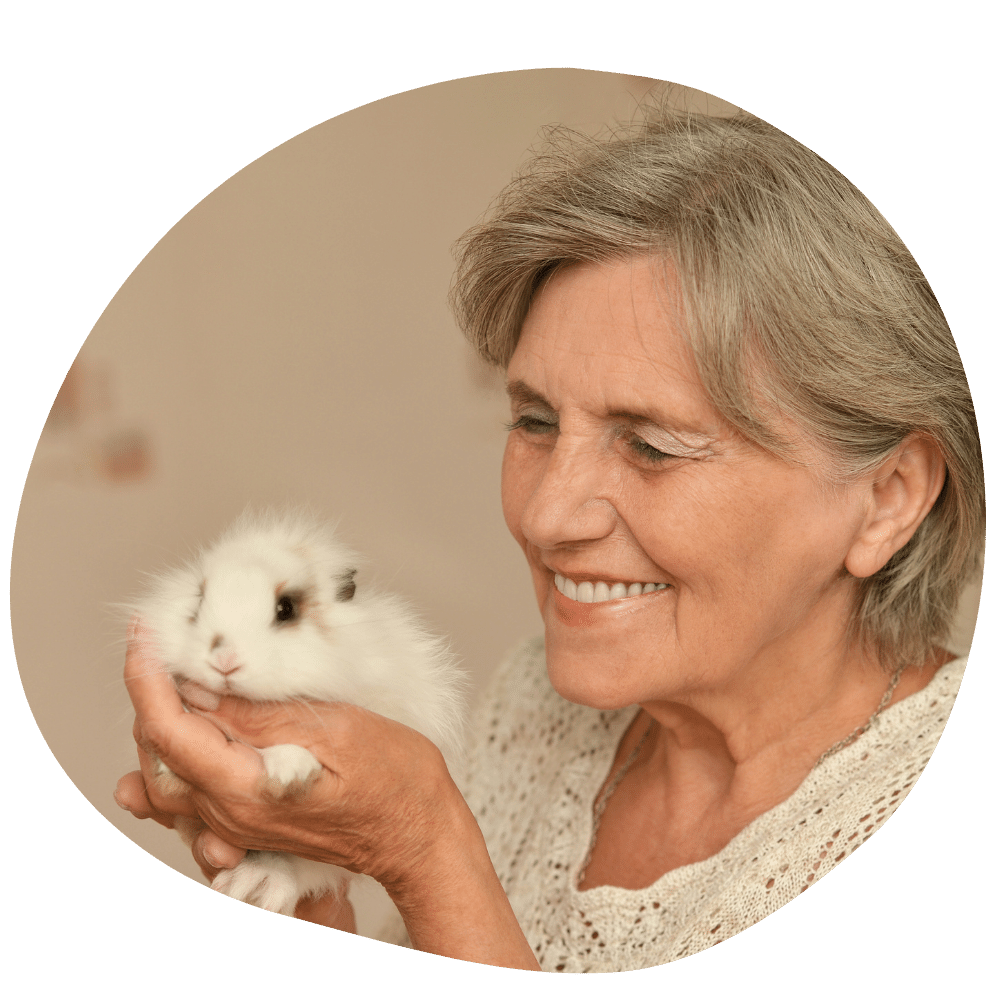 Elderly woman holding white rabbit with brown ears in her hands while smiling at him