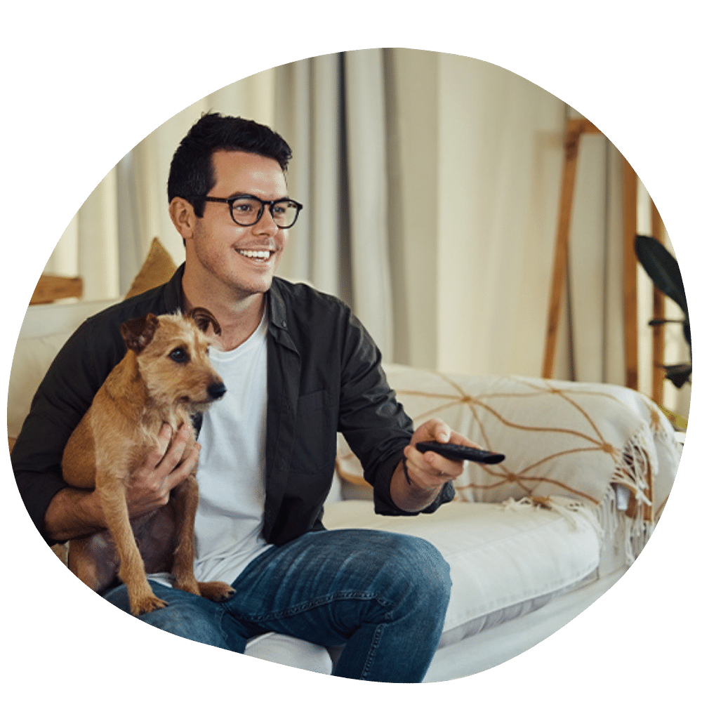 Man wearing blue shirt and white t shirt wearing glasses on couch holding brown down after dog sitter services