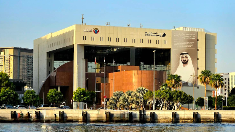 Dubai Municipality main entrance gate with official signage, full front view with water fountain in front, clear sky background in Dubai