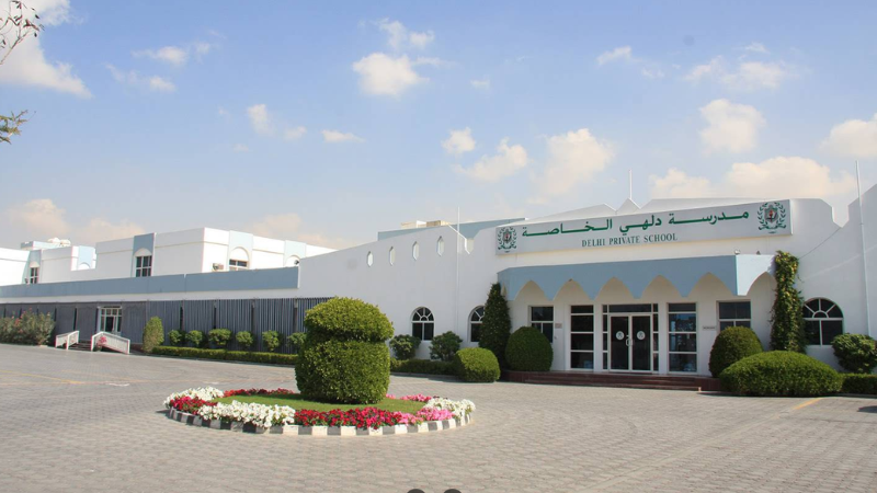 Full view of Delhi Private School Sharjah (DPS) main gate with road in front and flowers near the entrance area.