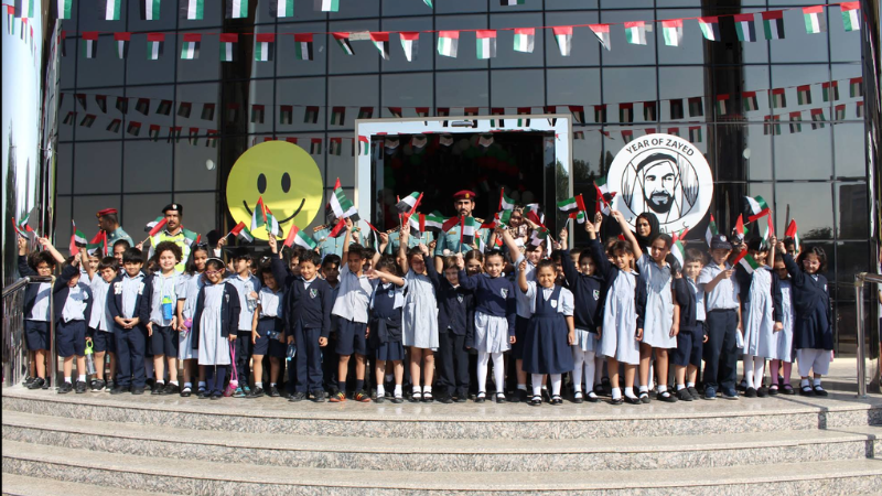 Students entering an English school through the gate with a security guard present for safety at one of the best schools in Sharjah.