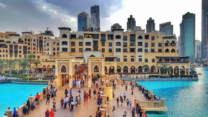 People walking around the Downtown Dubai lake with beautiful skyline views near Burj Khalifa and surrounding skyscrapers.