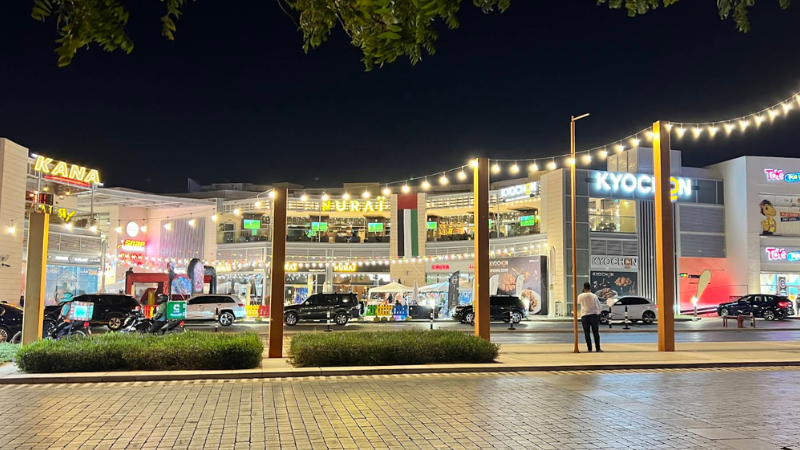 Dubai Motor City restaurant at night with parked cars and people enjoying the lively street atmosphere in a vibrant urban setting