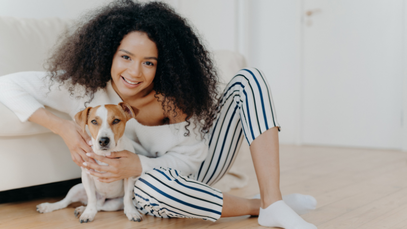 Dog sitter petting a happy dog while sitting on the floor at home.